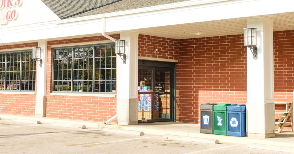 a trash, recycling and compost receptacle in front of a c-store